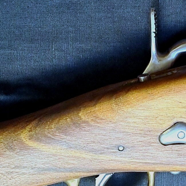 Dettaglio della contropiastra in ottone e della venatura del legno su un fucile ad avancarica artigianale