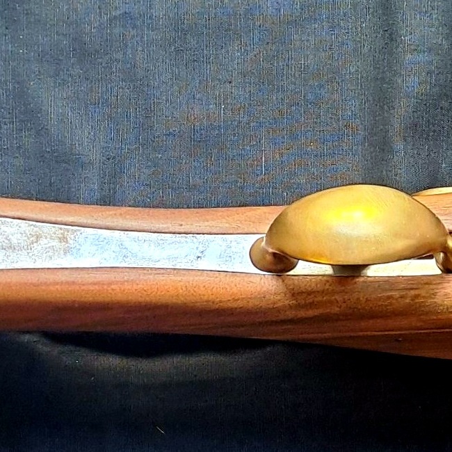 Dettaglio del ponticello in ottone e della venatura del legno su un fucile ad avancarica artigianale